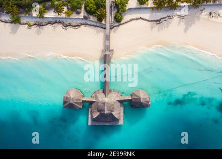 Photo aérienne de la cabane à pilotis avec un toit de chaume de palmier lavé avec des vagues de l'océan Indien turquoise sur la plage de sable blanc de l'île de Zanzibar, Tanza Banque D'Images