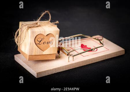 Une boîte avec le mot amour placé dans un mousetrap. Amour pour une personne avec de mauvaises intentions. Arrière-plan sombre. Banque D'Images