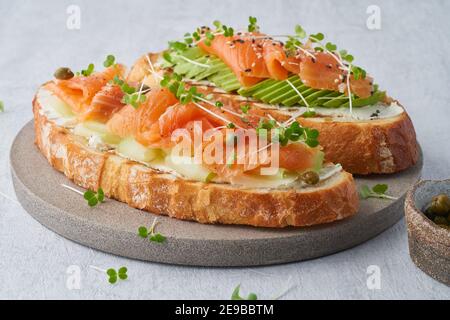 Deux sandwichs ouverts, pain grillé au saumon, fromage à la crème, avocat, tranches de concombre sur une table en béton blanc. Banque D'Images