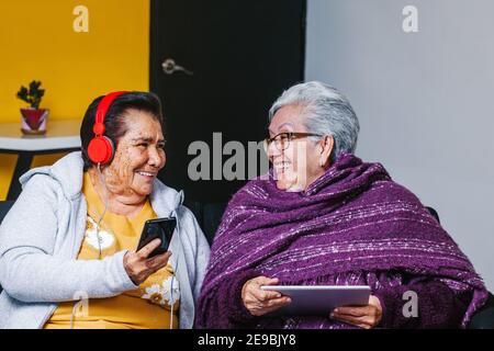 Latino Senior femmes écoutant de la musique avec des écouteurs à la maison dans la ville de Mexico, peuple mexicain Banque D'Images