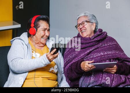 Latino Senior femmes écoutant de la musique avec des écouteurs à la maison dans la ville de Mexico, peuple mexicain Banque D'Images