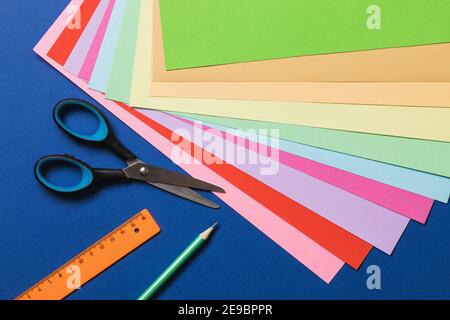 Papier et outils de couleur sur fond bleu, vue de dessus. Banque D'Images