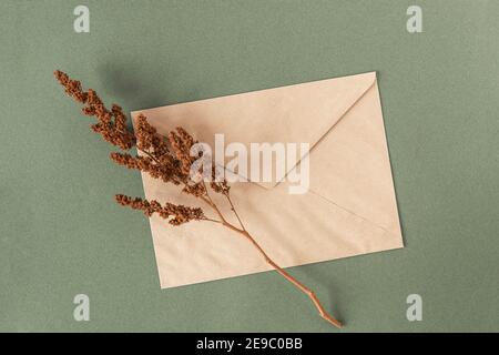 Enveloppe artisanale et fleurs sèches plantent sur fond vert. Vue de dessus Flat lay. Banque D'Images