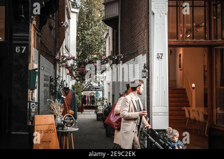 Amsterdam très animée jolie scène de rue avec une allée pittoresque entre les deux les magasins menant à la boutique de vêtements couple avec poussette enfant marche Banque D'Images