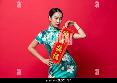 Femme asiatique portant une robe de cheongsam orientale présentant le label chinois du nouvel an dans le fond rouge isolé de studio, le texte signifie souhaiter de prospérité Banque D'Images