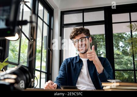 Souriant homme caucasien vlogger donner des pouces vers le haut tout en enregistrant la vidéo clip avec carmera à la maison pour le partager sur les réseaux sociaux Banque D'Images