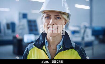 Portrait d'un beau sourire sur une femme d'appareil photo en gilet de sécurité et casque de sécurité. Femme professionnelle travaillant dans l'usine de fabrication moderne Banque D'Images