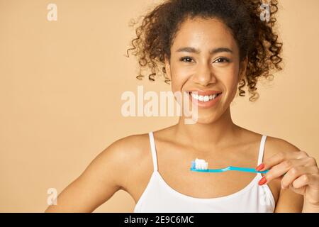 Portrait d'une jeune femme de race mixte gaie se brossant les dents le matin, posant isolée sur fond beige. Concept de soins dentaires Banque D'Images