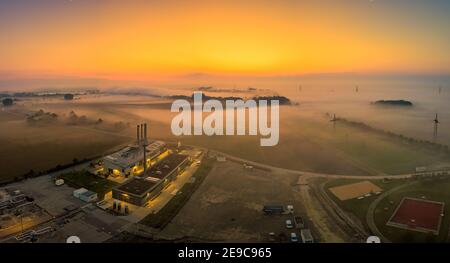 Vue aérienne d'un lever de soleil brumeux au-dessus d'une zone industrielle avec une usine. Brouillard surgelé sur un champ à côté d'un lac, lever de soleil tôt le matin. Banque D'Images