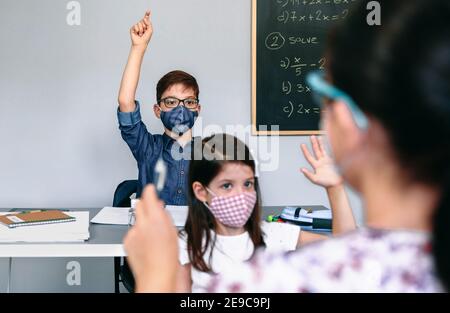 Les élèves avec des masques levant les mains à l'école Banque D'Images