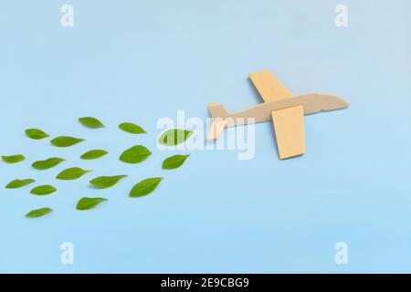 Modèle d'avion en bois émettant des feuilles vertes fraîches sur fond bleu. Les voyages durables; l'énergie propre et verte; et le biocarburant pour l'industrie aéronautique Banque D'Images