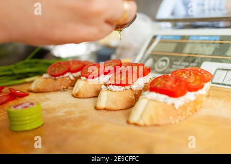 Bruschetta aux tomates, fromage de Philadelphie, saucisse fumée, aneth et huile d'olive. L'homme verse de l'huile à la bruschetta. Banque D'Images