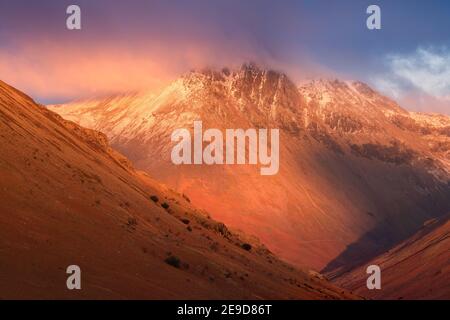 Majestueuses montagnes enneigées avec des nuages sombres et spectaculaires et une lumière rouge d'hiver. Arrière-plan de la nature. Lake District National Park, Royaume-Uni. Banque D'Images