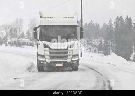 Camion semi-remorque White Scania en marche avant sur une route étroite et tordue lors d'une journée de neige hivernale. Salo, Finlande. 22 janvier 2021. Banque D'Images