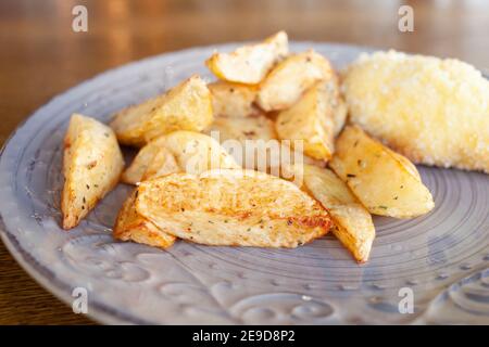 Pommes de terre cuites avec herbes et côtelettes en panure avec fromage et beurre. Nourriture sur une assiette en argile dans un café. Petit déjeuner, déjeuner et dîner au restaurant. Banque D'Images