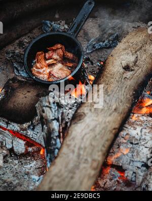 Vue de dessus de près du bacon cuit sur la cuisinière sur un feu de camp pendant le camping Banque D'Images