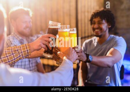 Quatre amis hommes heureux ivres assis dans un bar et de boire de la bière, se clinquant avec leurs verres pleins de bière, Banque D'Images