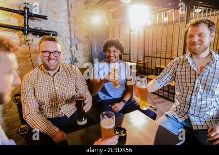 Groupe d'amis de sexe masculin assis au bar et buvant de la bière. S'amuser et sourire. Banque D'Images