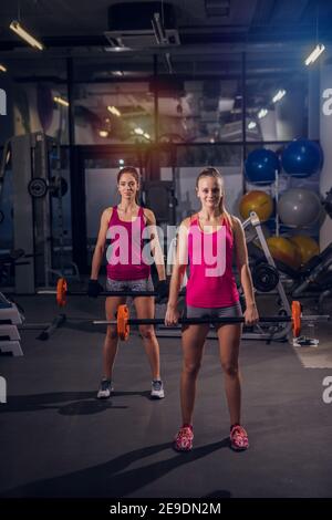 Deux jeunes filles fortes dans une salle de gym tenant des barres lourdes et regardant l'appareil photo. Banque D'Images