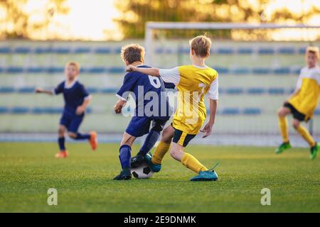 Enfants jouant au football. Groupe de jeunes garçons Kicking Soccer ball sur le terrain de stade. Les joueurs participent au match de football en deux équipes. Enfants en jaune an Banque D'Images