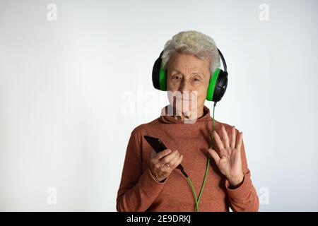 Femme plus âgée qui profite de la musique d'un smartphone. Porter un casque vert, en agitant avec sa main. Concept de technologie. Fond blanc. Banque D'Images
