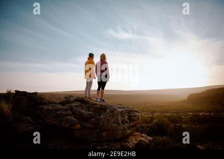 Vue arrière d'un jeune homme et d'une femme debout magnifique lever de soleil sur le sommet d'une falaise de montagne Banque D'Images