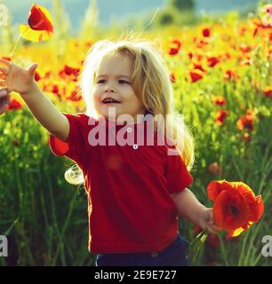 Enfant, petit garçon souriant dans un champ de fleurs de pavot avec tige verte sur fond naturel. L'été, les enfants s'amusent en plein air dans un magnifique jardin de printemps. Banque D'Images