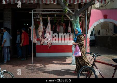 El Jadida, Maroc - 16 avril 2016 : une femme passant devant un boucher, dans la ville d'El Jadida. Banque D'Images