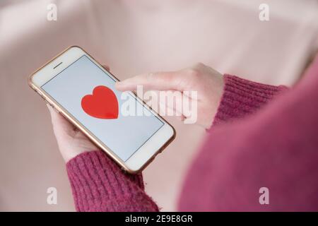 Une fille touchant un coeur sur l'écran tactile d'elle téléphone mobile pour aimer et trouver l'amour avec un en ligne application de datation Banque D'Images