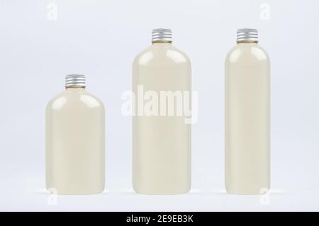 Assortiment de trois bouteilles hautes, basses et épaisses en plastique avec boisson fraîche pâle ou huile essentielle cosmétique, maquette de bouchon argenté sur fond blanc, templa Banque D'Images