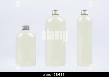 Assortiment de trois bouteilles hautes, basses et épaisses en plastique avec boisson fraîche pâle ou huile essentielle cosmétique, maquette de bouchon argenté sur fond blanc, templa Banque D'Images