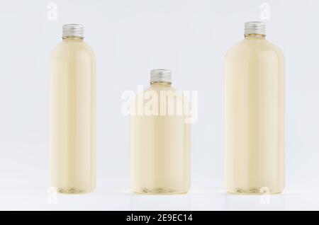 Assortiment de trois bouteilles hautes, basses et épaisses en plastique avec boisson fraîche pâle ou huile essentielle cosmétique, maquette de bouchon argenté sur fond blanc, templa Banque D'Images