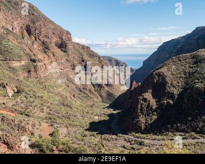 Barranco de Guayabonde avec ravin murs abrupts et chemin sinueux vers l'océan. Gran Canaria, île des Canaries, Espagne. Jour ensoleillé, ciel bleu, nuages blancs Banque D'Images