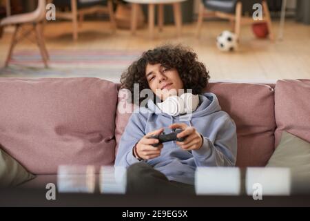 Adolescent dans un casque sans fil reposant sur un canapé jouant à des jeux vidéo dans la chambre Banque D'Images