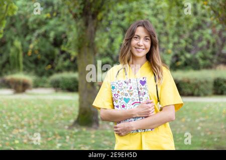 Jeune femme souriante infirmière avec un dossier de coeurs dans ses mains. Elle est à l'extérieur dans la nature. Espace pour le texte. Banque D'Images