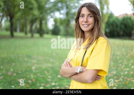 Portrait d'une infirmière caucasienne avec ses bras croisés dans une posture confiante. Elle est à l'extérieur. Espace pour le texte. Banque D'Images