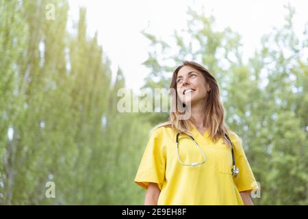 Portrait de jeune infirmière souriante avec stéthoscope regardant le ciel. Elle est à l'extérieur de la nature. Espace pour le texte. Banque D'Images