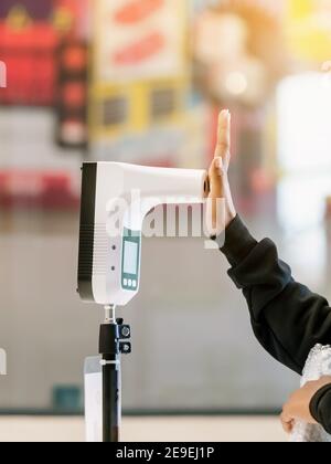 Client avec un masque de protection, main levée au thermomètre numérique avec appareil de balayage de la température pour détecter la fièvre avant d'entrer dans la zone. Le dépistage doit être effectué Banque D'Images