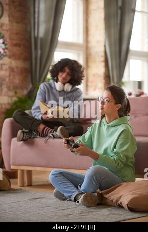 Deux adolescents se reposant à la maison jouant à des jeux vidéo et de lecture livres Banque D'Images