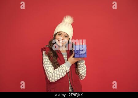 faites des choses agréables. joyeux enfant en hiver avec fond rouge. nouvelle année à venir. petit coffret cadeau pour enfant. bonne enfance. cadeaux de noël et souvenirs. préparez-vous pour les vacances d'hiver. Banque D'Images