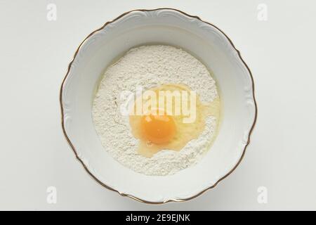 Photographie alimentaire, farine dans un bol et œufs biologiques sur fond blanc. Banque D'Images