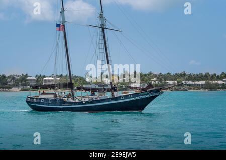 Key West, Etats-Unis - 04.30.2017: Personnes naviguant sur un yacht en bois avec voiles vers le bas. Stations tropicales et arbres en arrière-plan. Banque D'Images