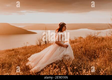 Bride on a summer field in white wedding dress rolling and dancing