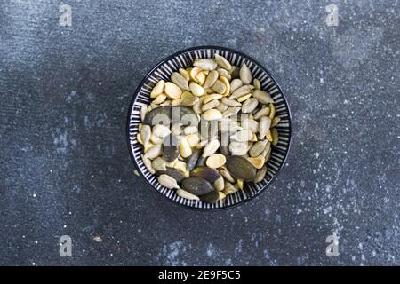 Vue de dessus des graines de tournesol et de citrouille dans un bol sur une surface bleue Banque D'Images