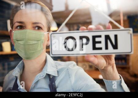 Femme propriétaire de petite entreprise portant masque tournant rond Ouvrir l'affiche pendant une pandémie de santé Banque D'Images