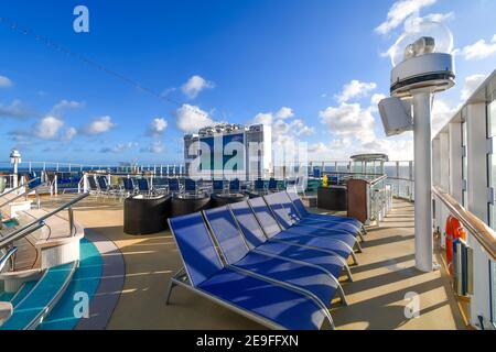 Un pont supérieur de bateau de croisière vide avec écran multimédia et chaises longues en mer par une journée ensoleillée. Banque D'Images