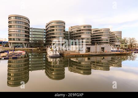 Duisburg, NRW, Allemagne, 04 février 2021. Par une journée ensoleillée et sans vent, l'eau complètement encore reflète les bâtiments de l'arrière-port de Duisburg, ici le bâtiment des cinq bateaux. Tandis que les rives du Rhin ont inondé, les choses sont beaucoup plus calmes et plus calmes à l'Innenhafen (port intérieur) qui est alimenté par le Rhin. La région était autrefois le port central et le point de commerce de la ville, aujourd'hui réaménagé en logements, centres culturels, centres technologiques et médiatiques et un espace de loisirs. Le port moderne de Duisburg est maintenant situé à Ruhrort à proximité, l'un des plus grands ports fluviaux d'Europe. Banque D'Images