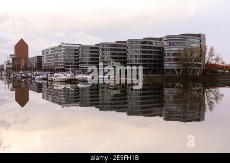 Duisburg, NRW, Allemagne, 04 février 2021. Par une journée ensoleillée et sans vent, l'eau complètement encore reflète les bâtiments de l'arrière-port de Duisburg, ici le bâtiment des cinq bateaux. Tandis que les rives du Rhin ont inondé, les choses sont beaucoup plus calmes et plus calmes à l'Innenhafen (port intérieur) qui est alimenté par le Rhin. La région était autrefois le port central et le point de commerce de la ville, aujourd'hui réaménagé en logements, centres culturels, centres technologiques et médiatiques et un espace de loisirs. Le port moderne de Duisburg est maintenant situé à Ruhrort à proximité, l'un des plus grands ports fluviaux d'Europe. Banque D'Images