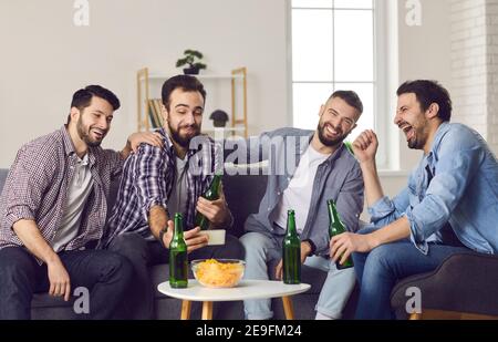 Souriant, des amis enthousiastes boivent de la bière, mangent des en-cas et font du selfie pendant la fête à la maison Banque D'Images