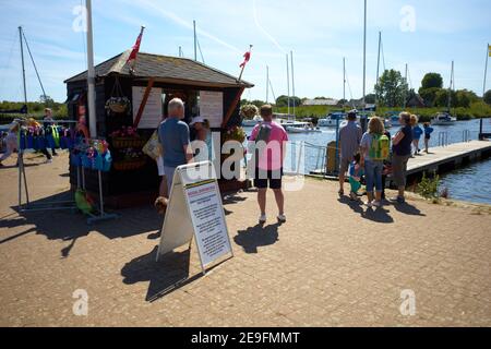 Photographie des gens qui font la queue pour des billets de location de bateaux au port de Christchurch, Devon, Royaume-Uni. L'enseigne de distance sociale est placée devant la billetterie. Banque D'Images